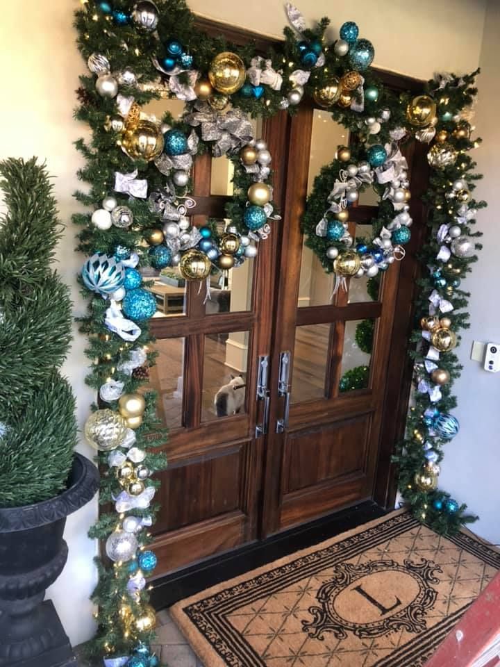 Double doors decorated with festive greenery, blue and gold ornaments, and wreaths, leading to a home with an 