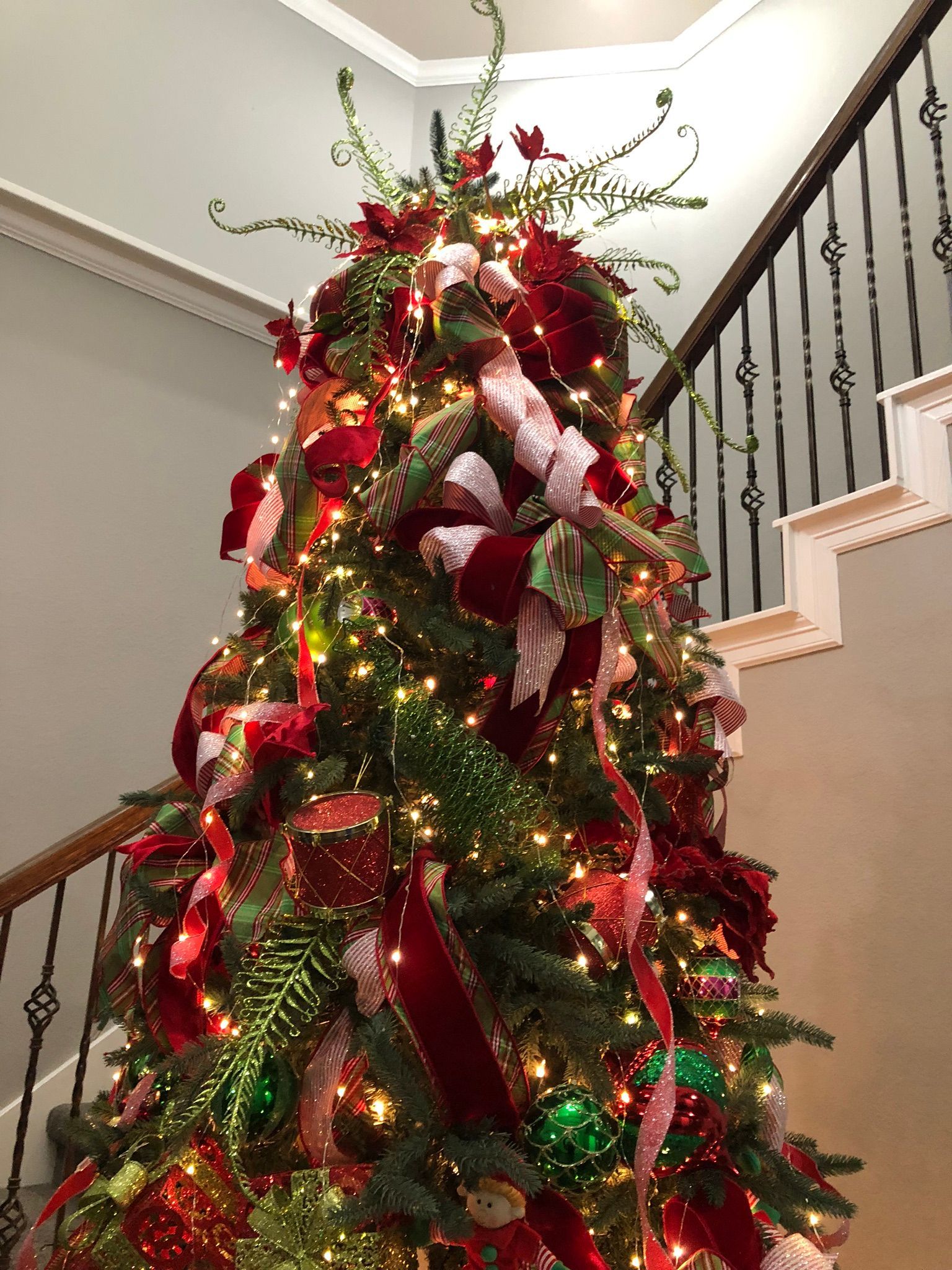A decorated Christmas tree with red ribbons, ornaments, and greenery, positioned next to a staircase.