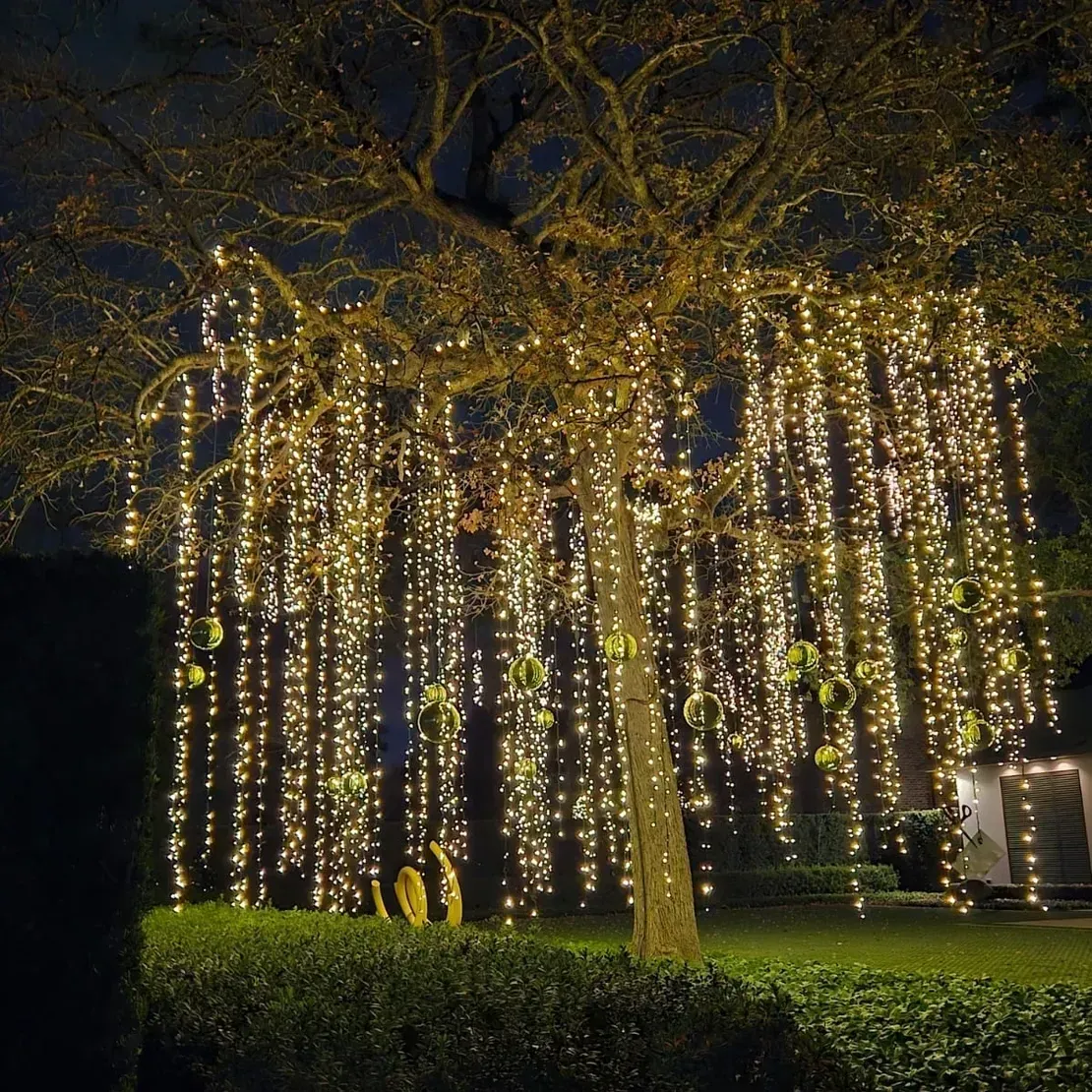 A black front door of a gray stone building decorated with Christmas garland, red bows, silver ornaments, and a wreath.