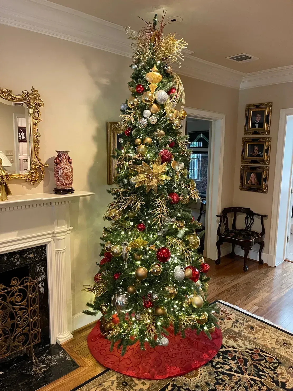 A tall, decorated Christmas tree in a living room with a red tree skirt, gold ornaments, and warm lights.