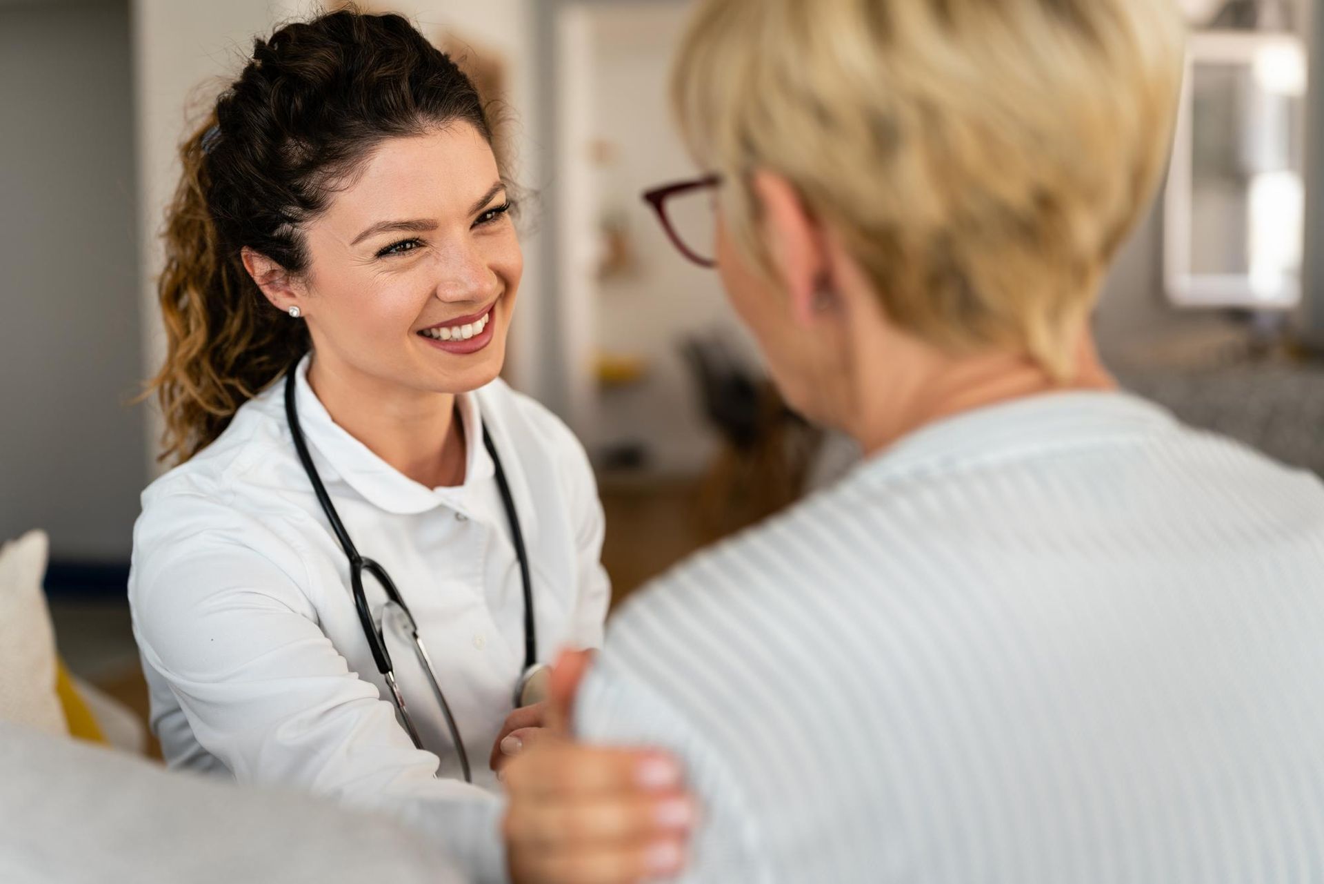 Smiling medical professional with stethoscope consoles a patient indoors.