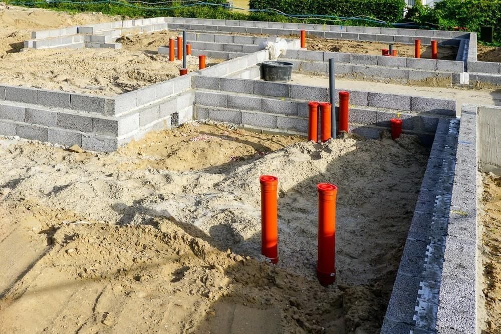 A foundation of a house under construction with red pipes in the sand.