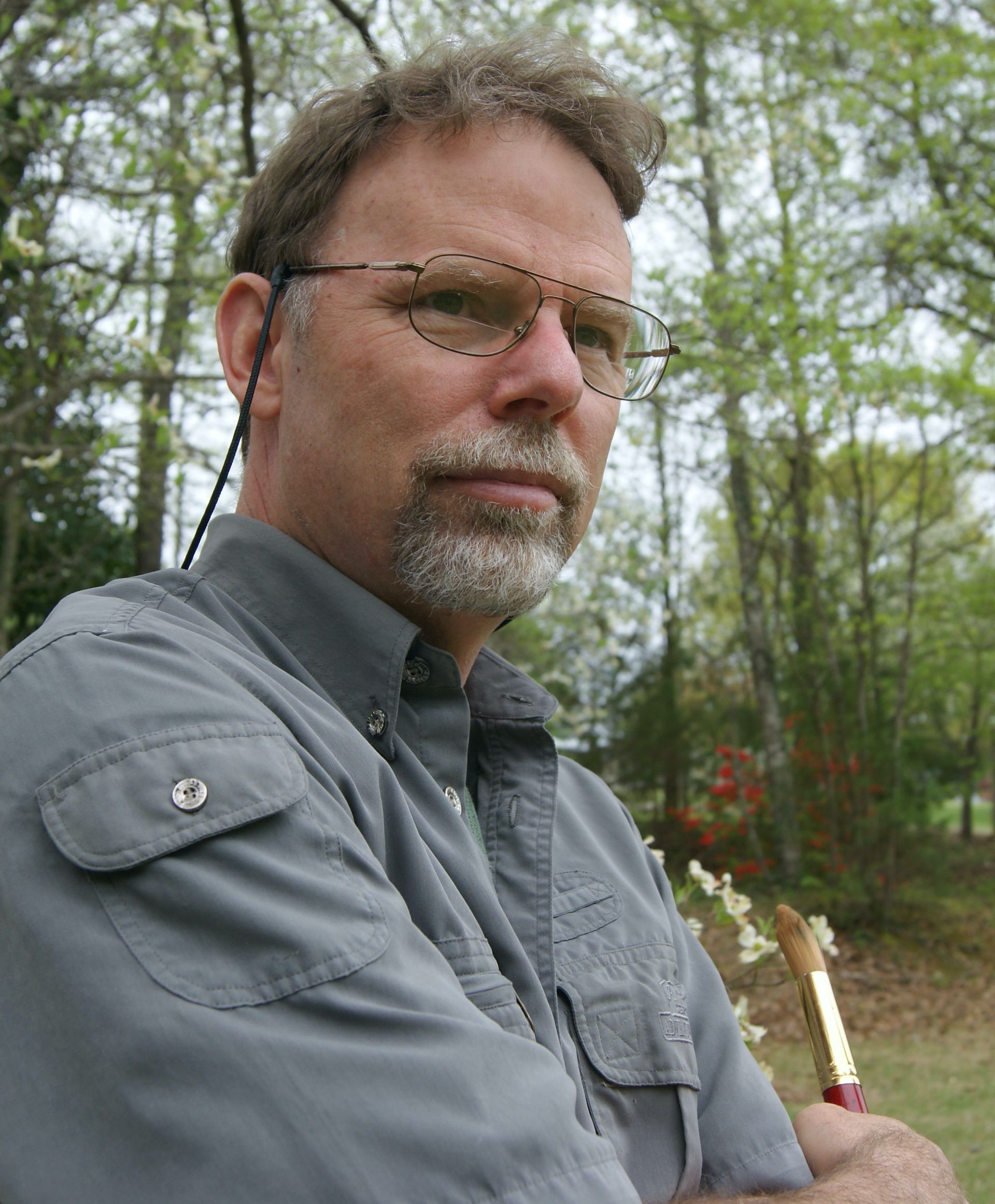 Artist Dr. Russell Jewell with glasses and a beard is holding a brush