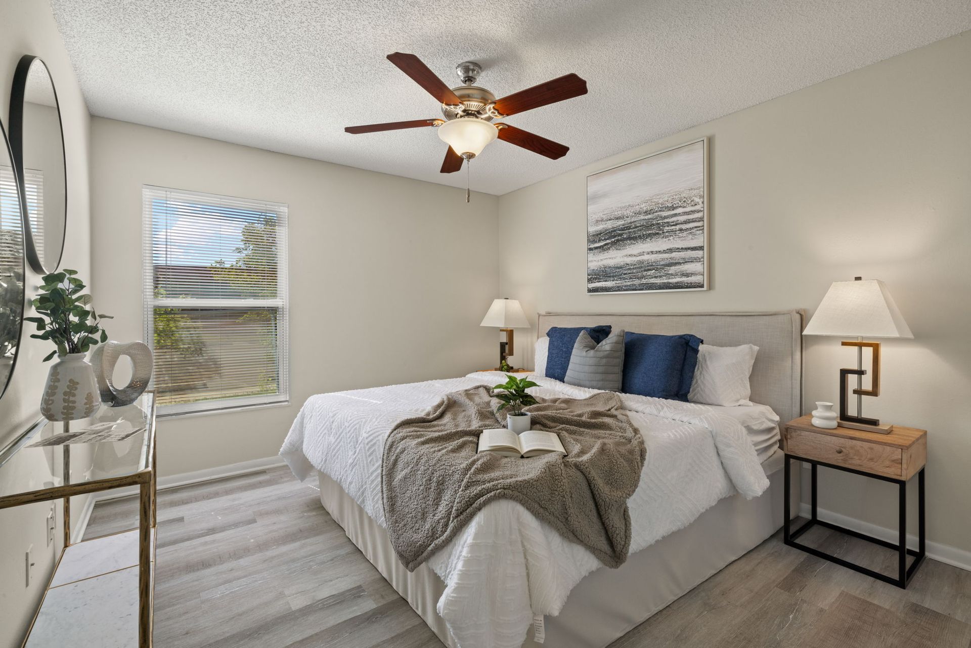 Bedroom with bed, nightstands, window, ceiling fan, artwork, and wood-look flooring.