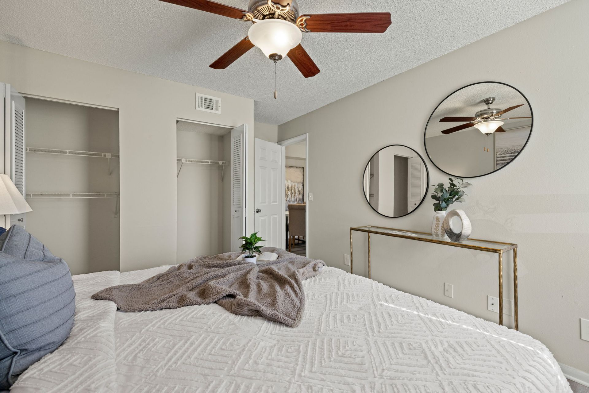 Bedroom with bed, closets, ceiling fan, and round mirrors above a mirrored console.
