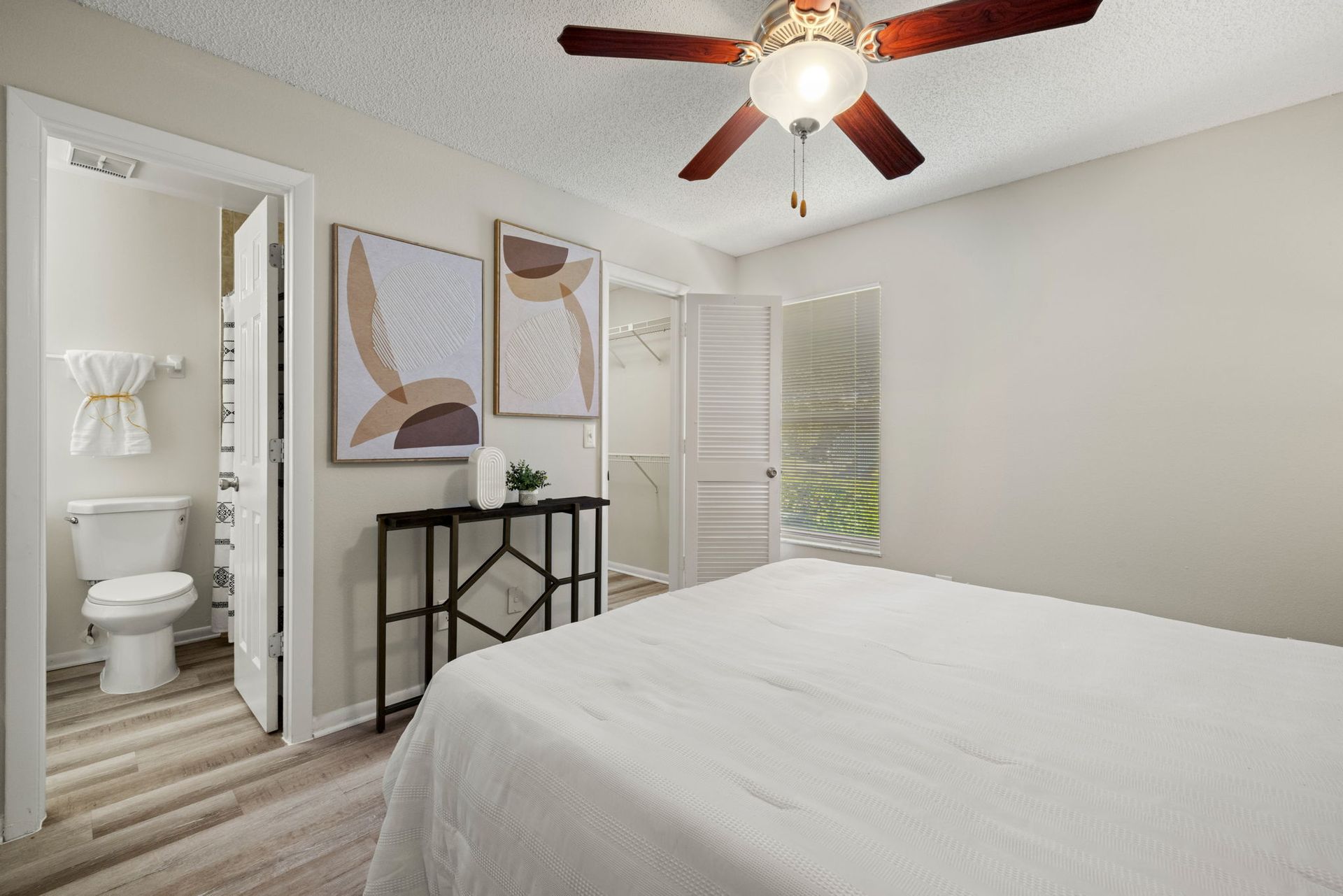 Bedroom with a bed, small bathroom, and decorative artwork on the wall. Ceiling fan visible.