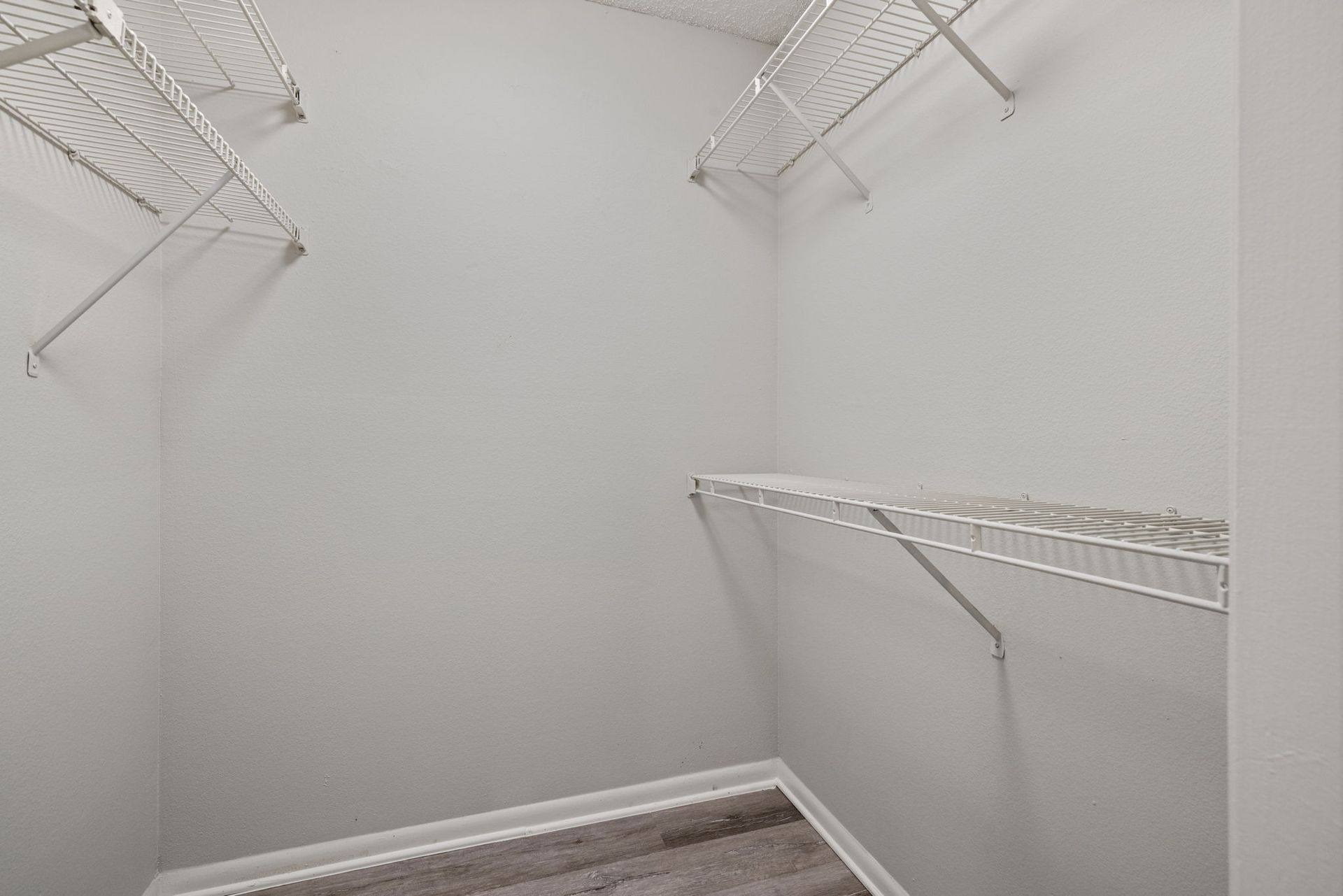 Empty walk-in closet with white wire shelving on white walls. Gray flooring.