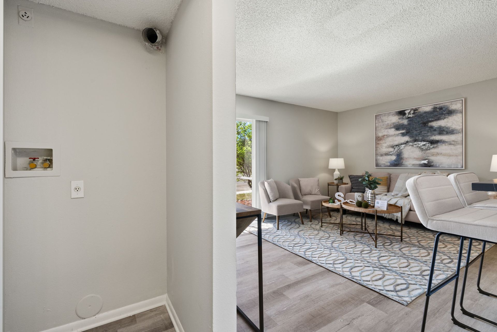 Laundry area and living room doorway; light gray walls, open to living room with seating, rug, and artwork.