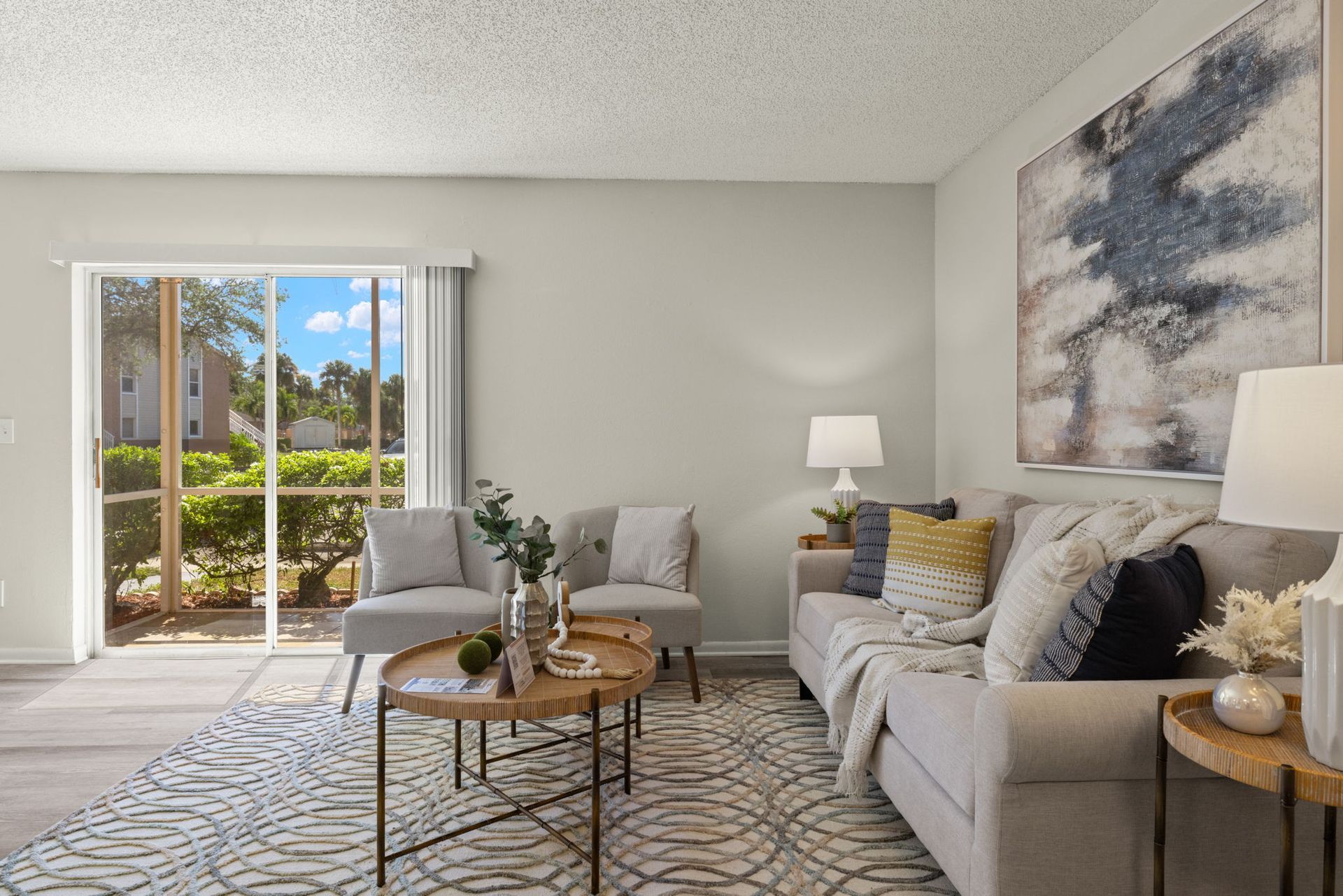 Living room with couch, chairs, coffee table, rug, sliding glass door, and artwork.
