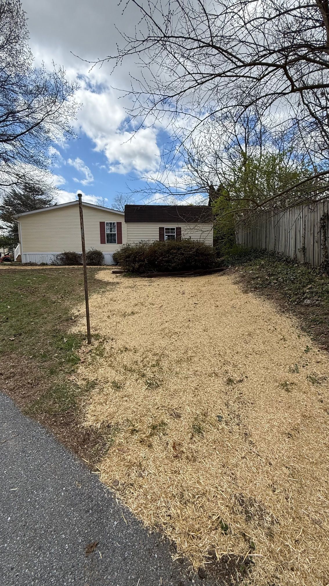 Tan house with brown roof, a gravel driveway, and a cloudy sky.