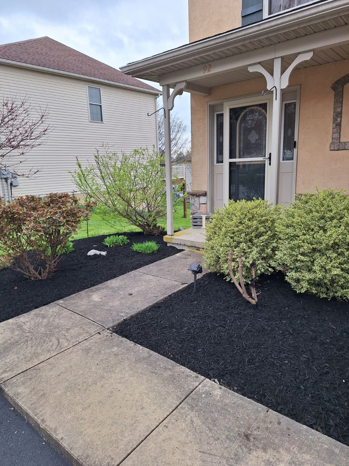 A house exterior with a sidewalk leading to the front door. Landscaping includes black mulch and bushes.