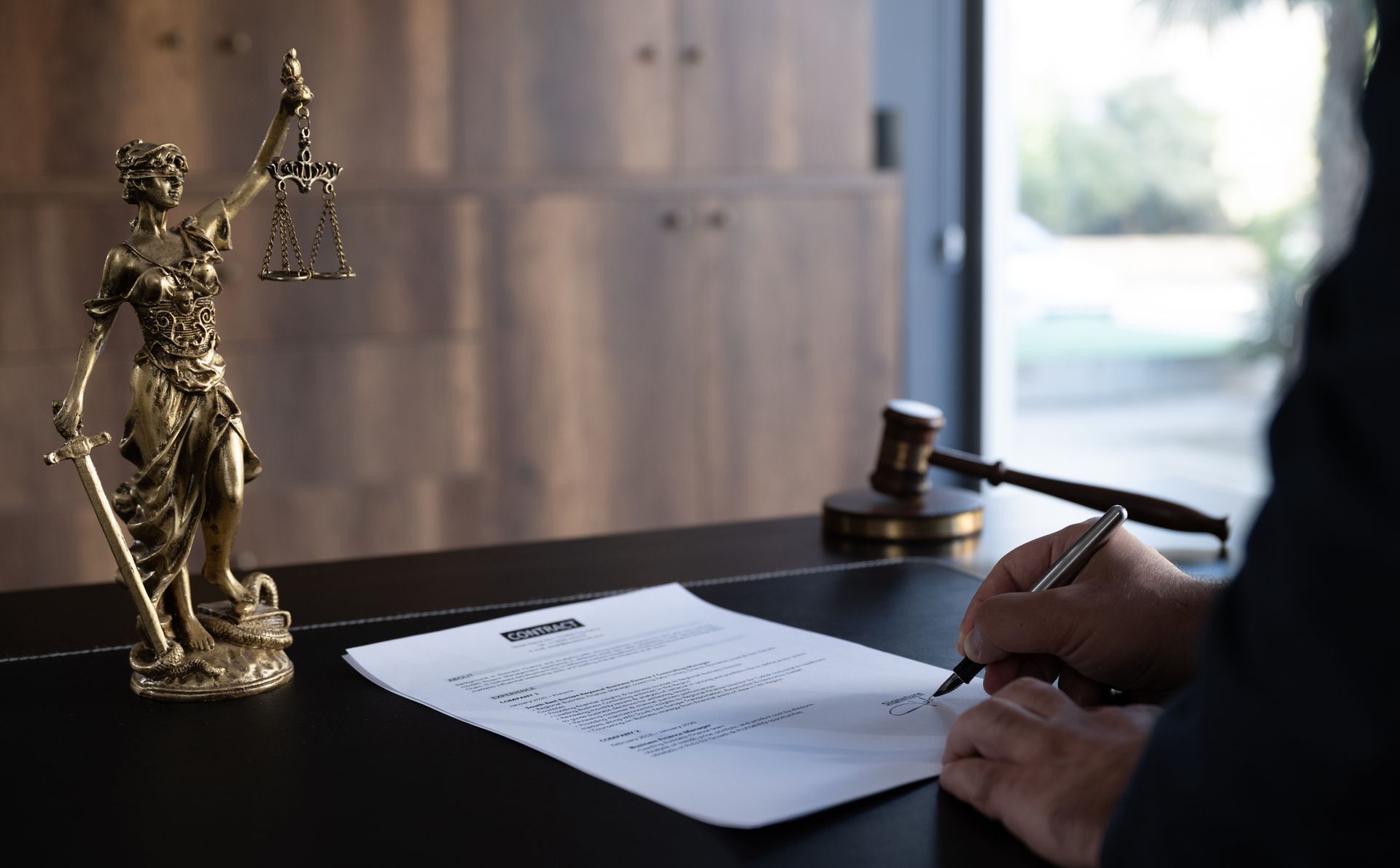 A person is signing a document in front of a statue of justice.