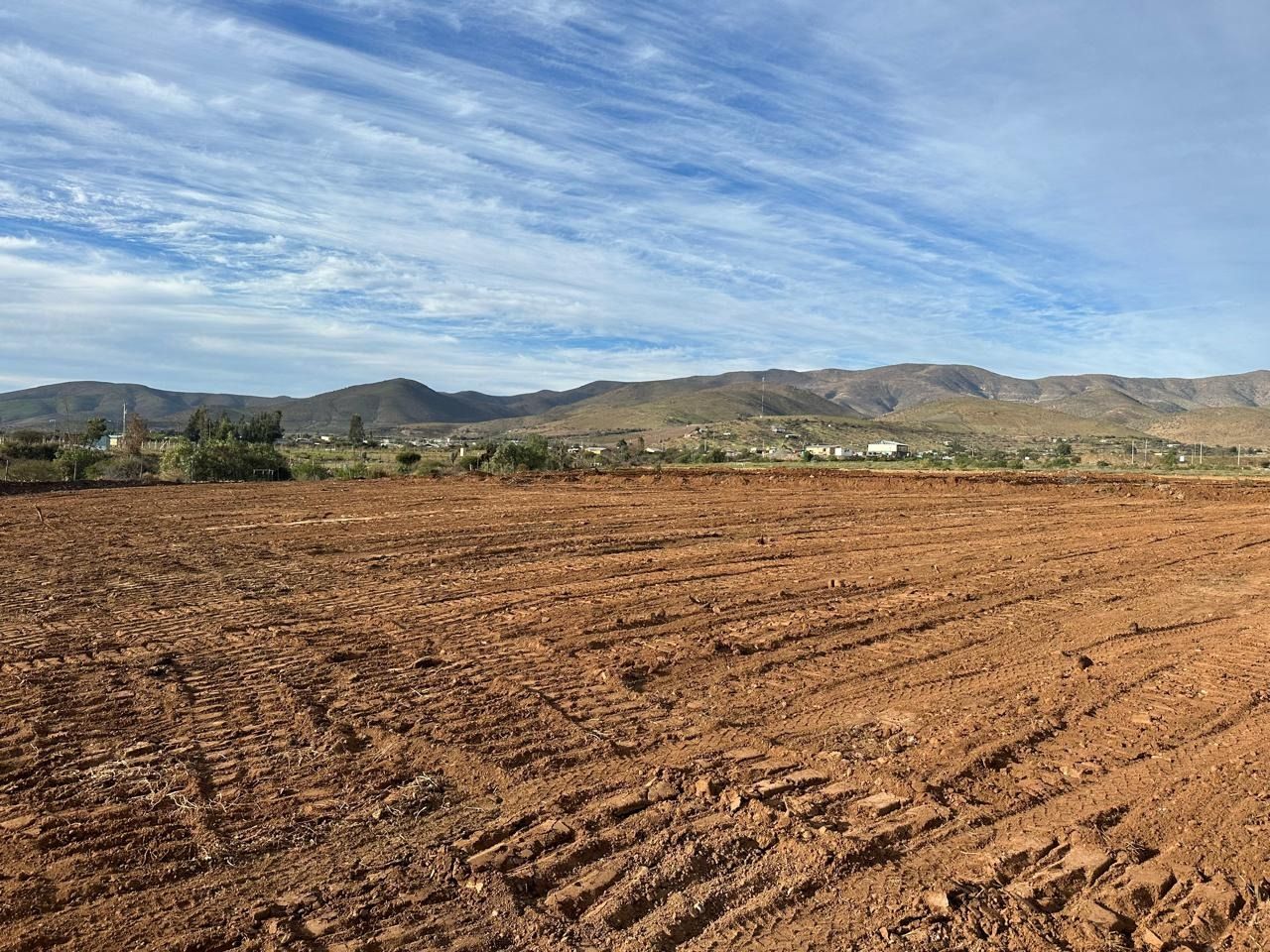 Un campo de tierra con montañas al fondo y un cielo azul con nubes.