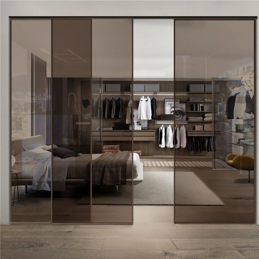Camera da letto con ante scorrevoli a specchio che riflettono la stanza e cabina armadio con vestiti.