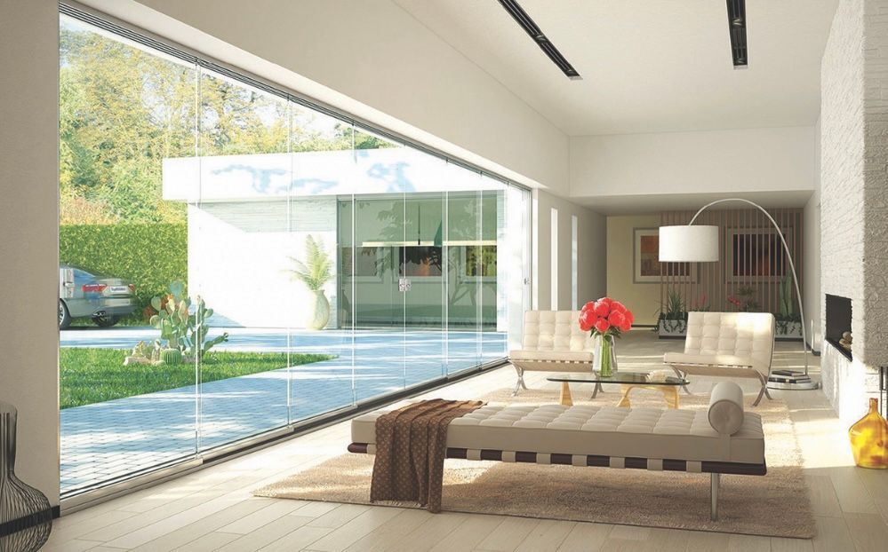 Moderno soggiorno con parete in vetro a tutta altezza, mobili bianchi, vista sul giardino e luce naturale.