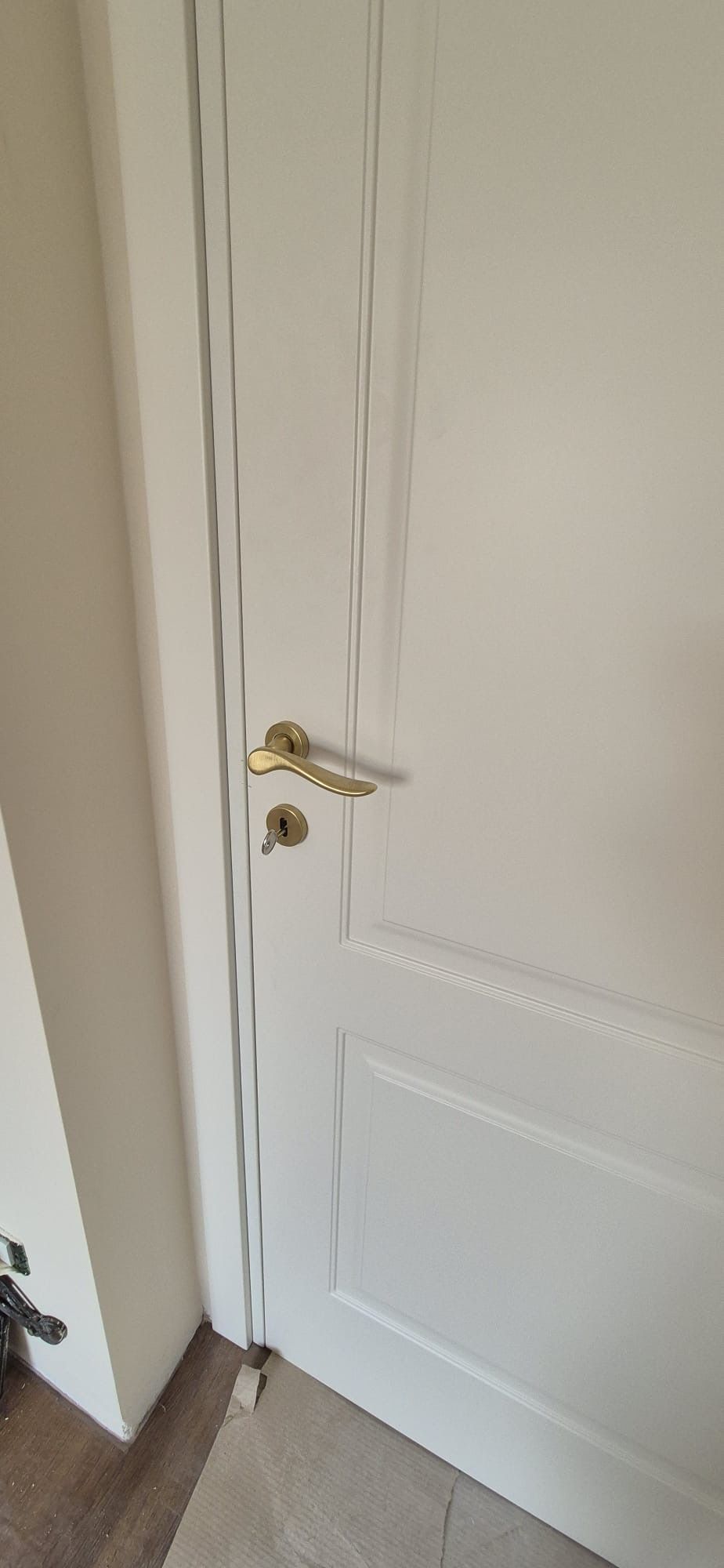 Porta bianca con maniglia e serratura in ottone, inserita in un interno dai colori chiari, accanto a una parete coordinata.