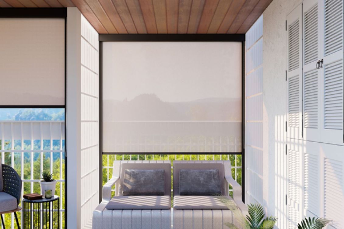 Balcone con tende bianche, posti a sedere e persiane parzialmente aperte. La luce del sole entra a fiotti.