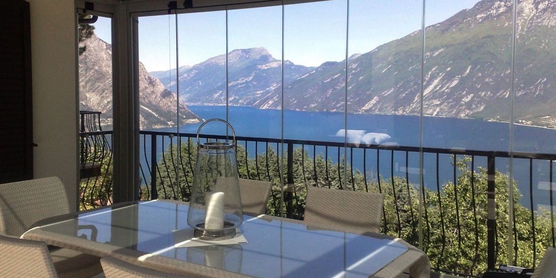 Un patio panoramico si affaccia sul lago e sulle montagne. All'interno, con pareti in vetro trasparente, si trovano un tavolo e sedie in vetro.