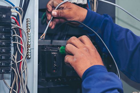 A man is working on an electrical box with a screwdriver.