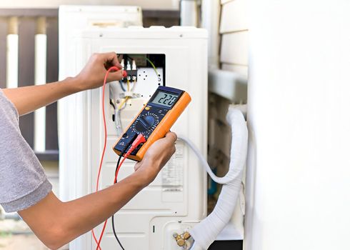 A man is using a multimeter to test an air conditioner.