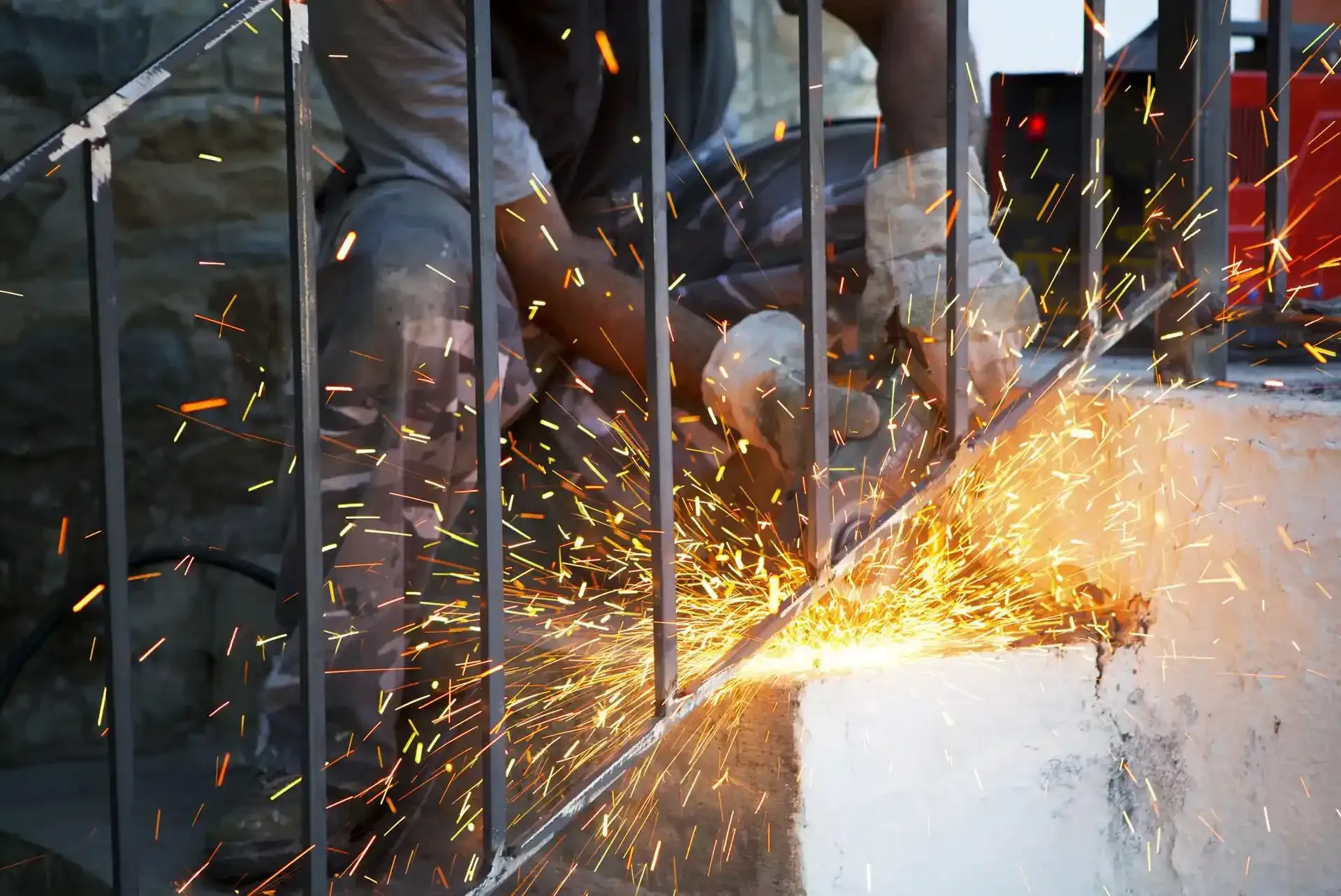 Una persona usa una smerigliatrice angolare per tagliare delle barre di metallo su un gradino di cemento, creando delle scintille.