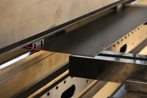 Una lamiera piegata da una macchina. La lamiera scura è tra due strutture metalliche.