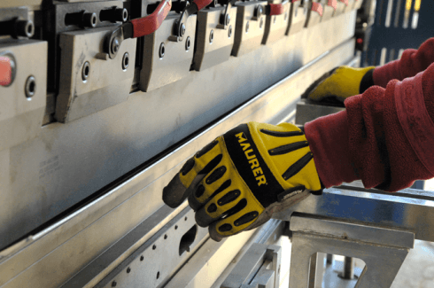Persona che indossa guanti gialli piega una lamiera con una macchina industriale.