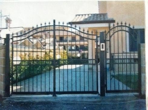 Cancelli d'accesso in ferro battuto nero, parte superiore arcuata con pinnacoli decorativi, chiusi.