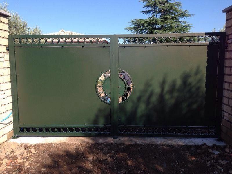 Cancello in metallo verde con maniglia circolare decorativa, incastonato tra pilastri in mattoni, all'esterno.