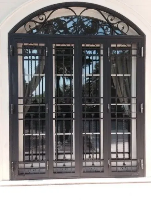 Finestra ad arco in metallo nero con quattro vetri e decorazioni in ferro battuto.