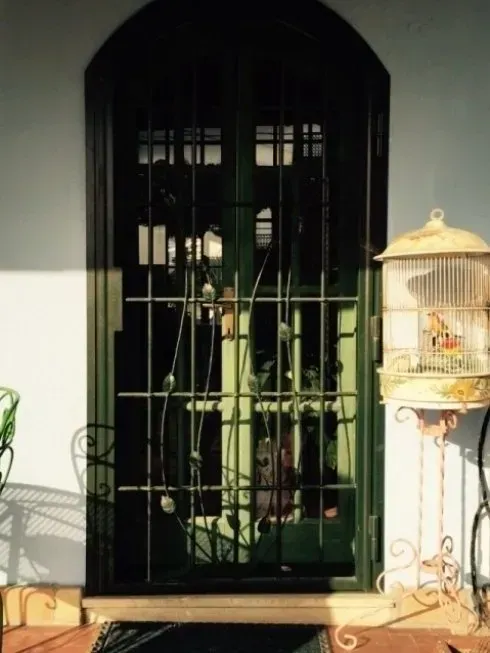 Porta ad arco verde con sbarre in ferro battuto e una gabbia per uccelli su un supporto.
