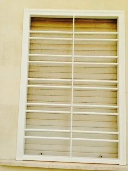 Finestra bianca con listelli orizzontali e divisori verticali, inserita in una parete beige chiaro.