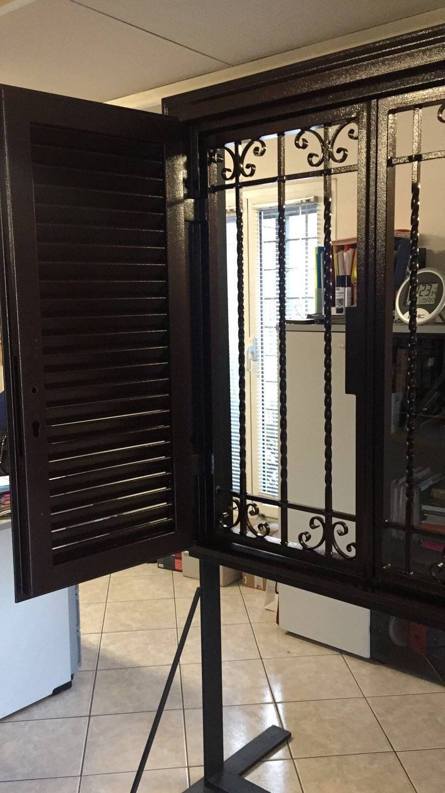 Finestra marrone con persiana aperta e inferriate decorative in ferro battuto.