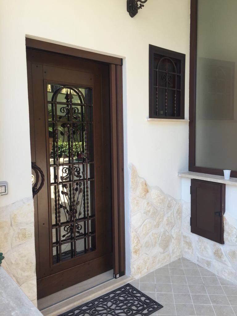 Porta d'ingresso in legno con elementi decorativi in ​​ferro battuto, accanto a una piccola finestra e a una sezione di muro in pietra.