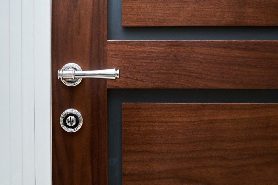 Primo piano di una moderna porta in legno con maniglia e serratura argentate, pannelli in legno marrone scuro e finiture bianche.