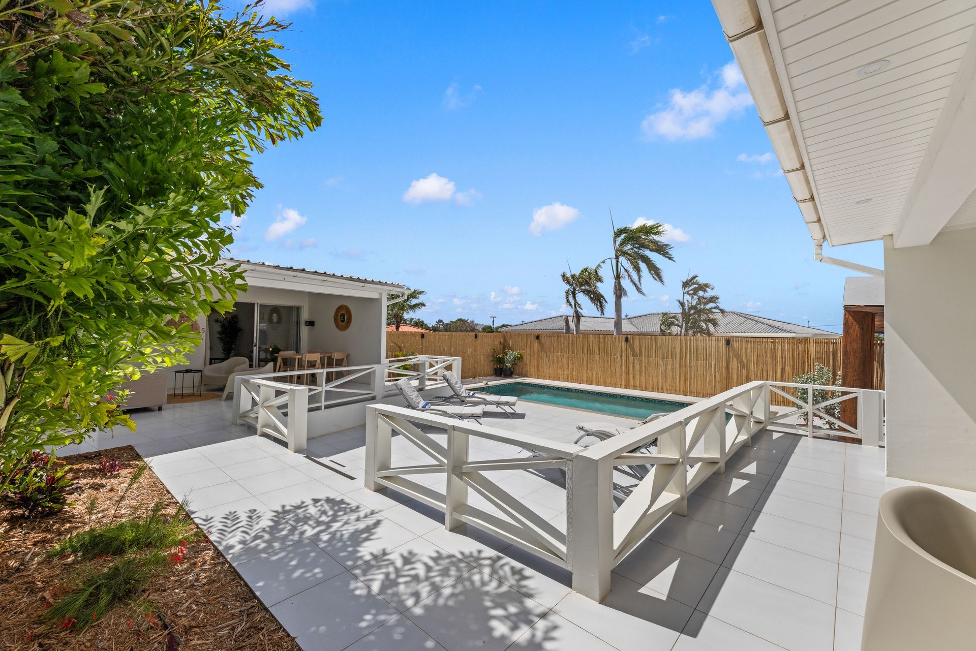 Patio with seating, table, and decorative straw hanging, overlooking a sunny outdoor area and blue sky.