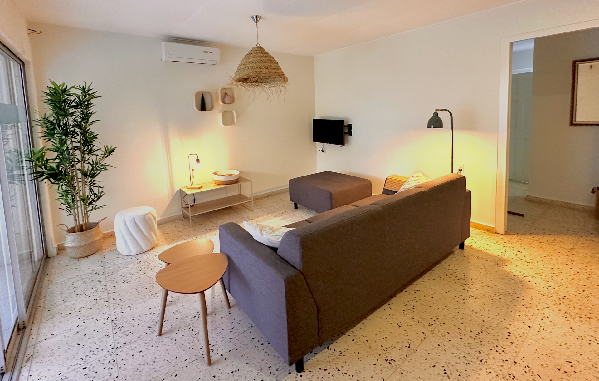 Bright, modern living room with a gray sofa, small tables, and a large plant.