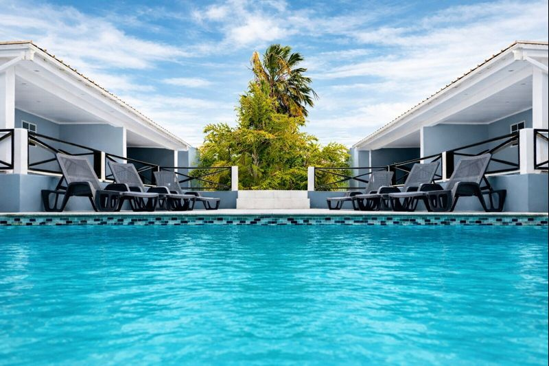 Pool with lounge chairs between two buildings, blue sky.