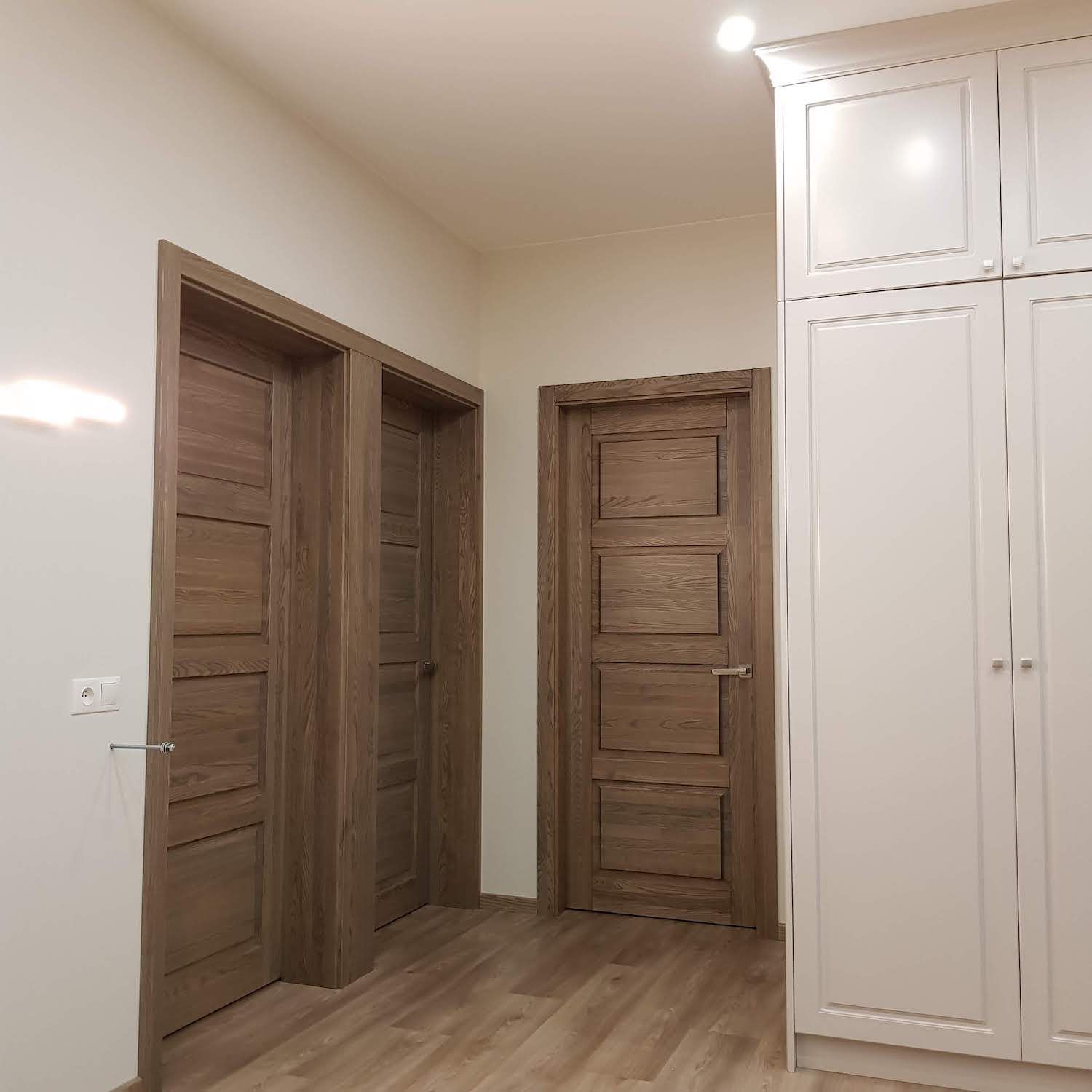 Prieškambaris su medinėmis durimis ir baltomis spintelėmis
