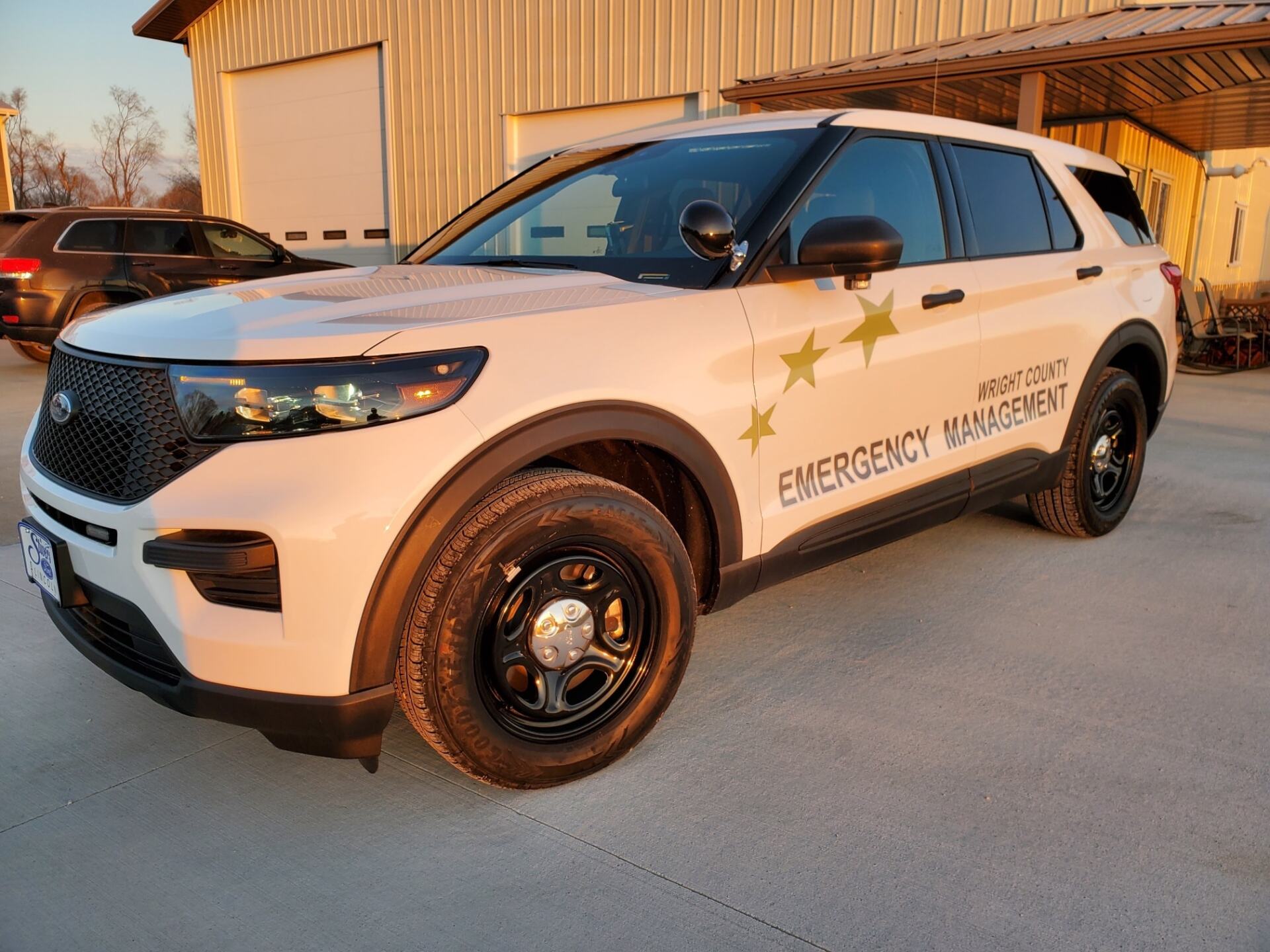 A white emergency management vehicle is parked in front of a building.