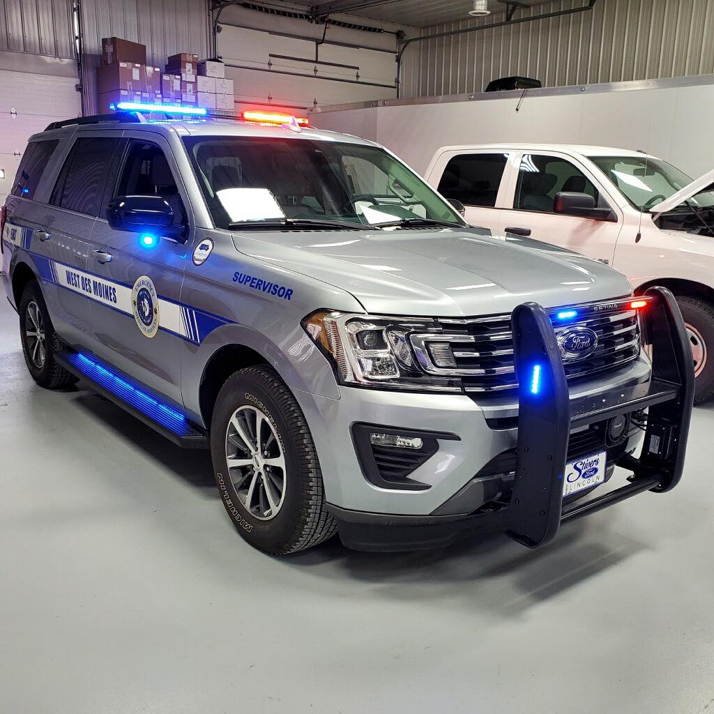 A police car is parked in a garage next to a white truck.