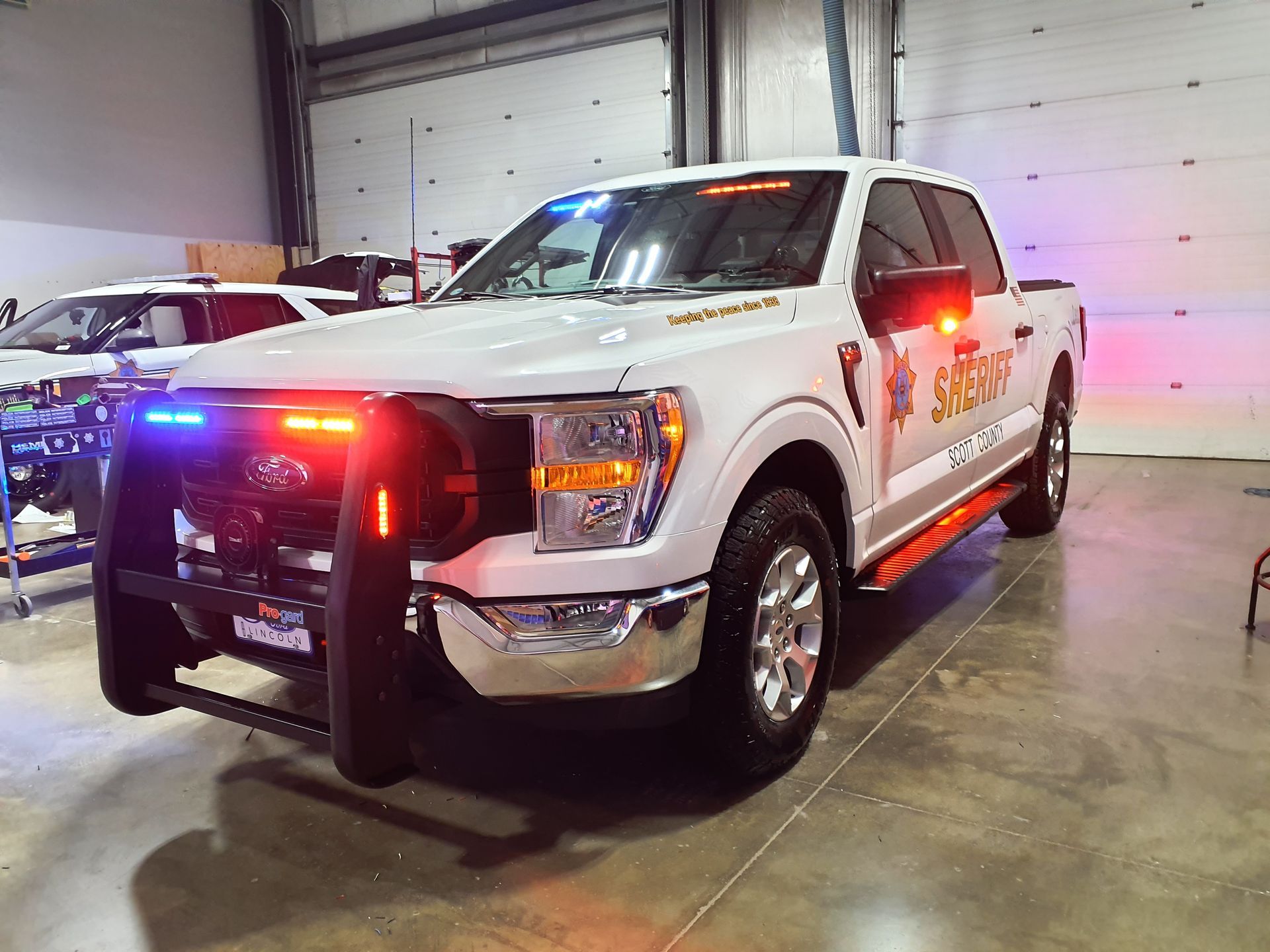 A white truck with red and blue lights on the front is parked in a garage.