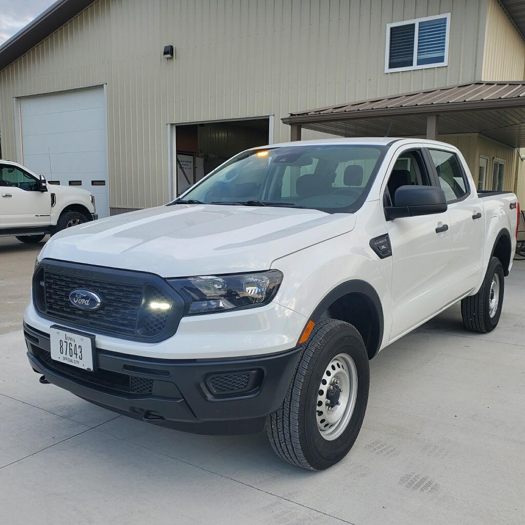 A white ford ranger truck is parked in front of a building.