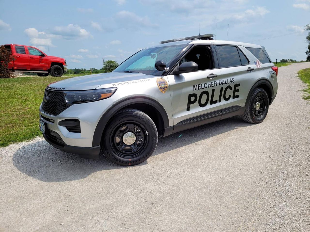 A silver police car is parked on the side of a gravel road.