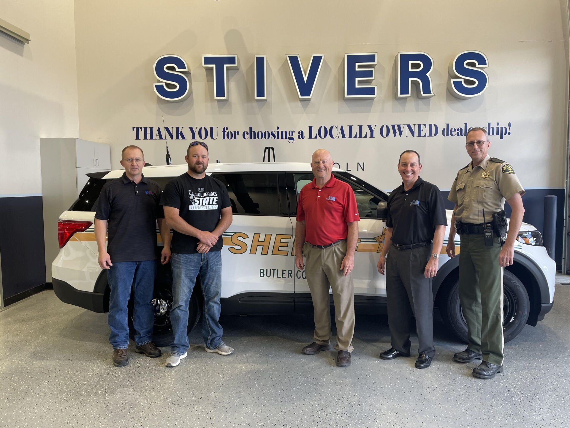 A group of men are posing for a picture in front of a sheriff 's car.