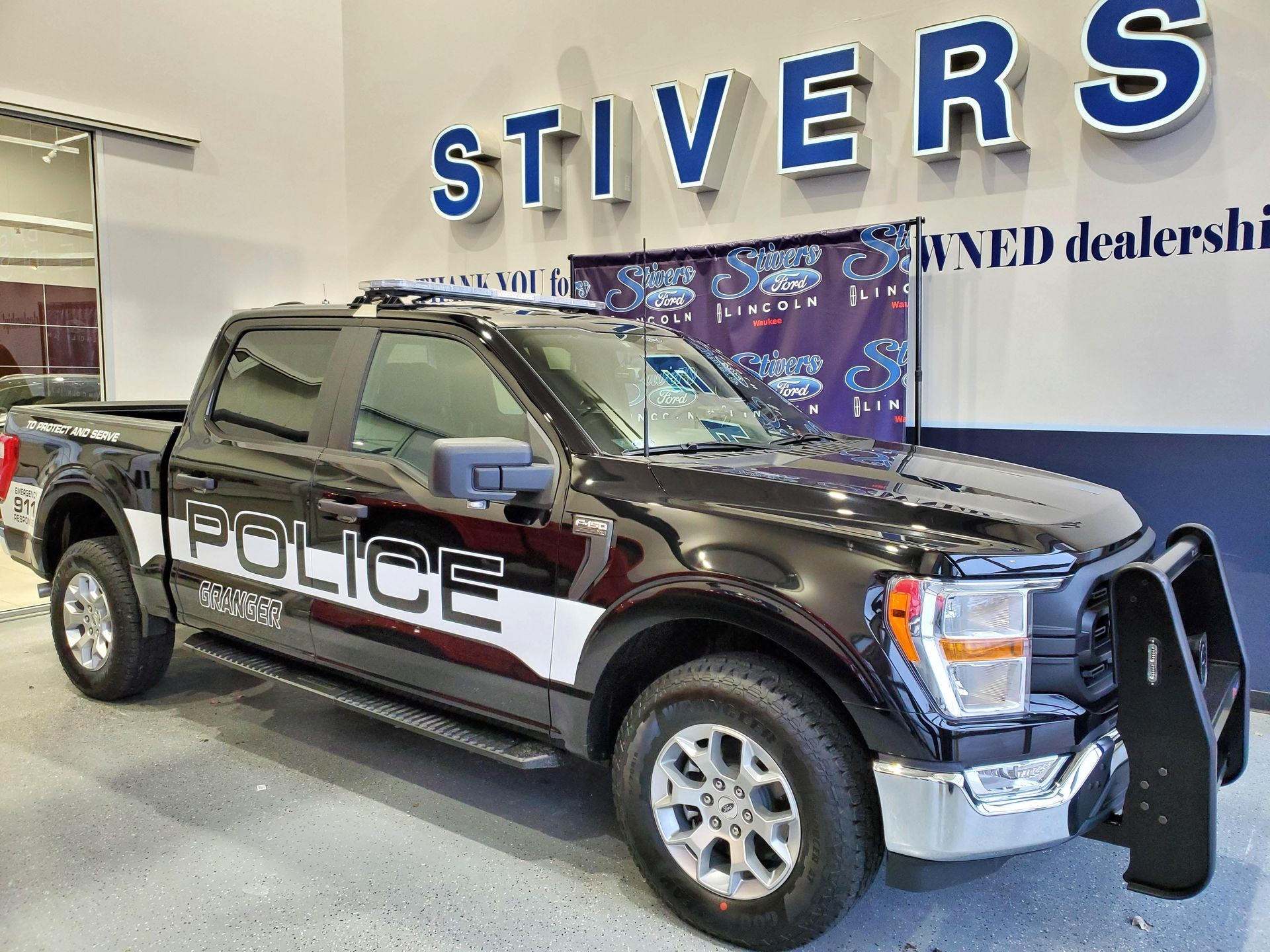 A black and white police truck is parked in front of a dealership.