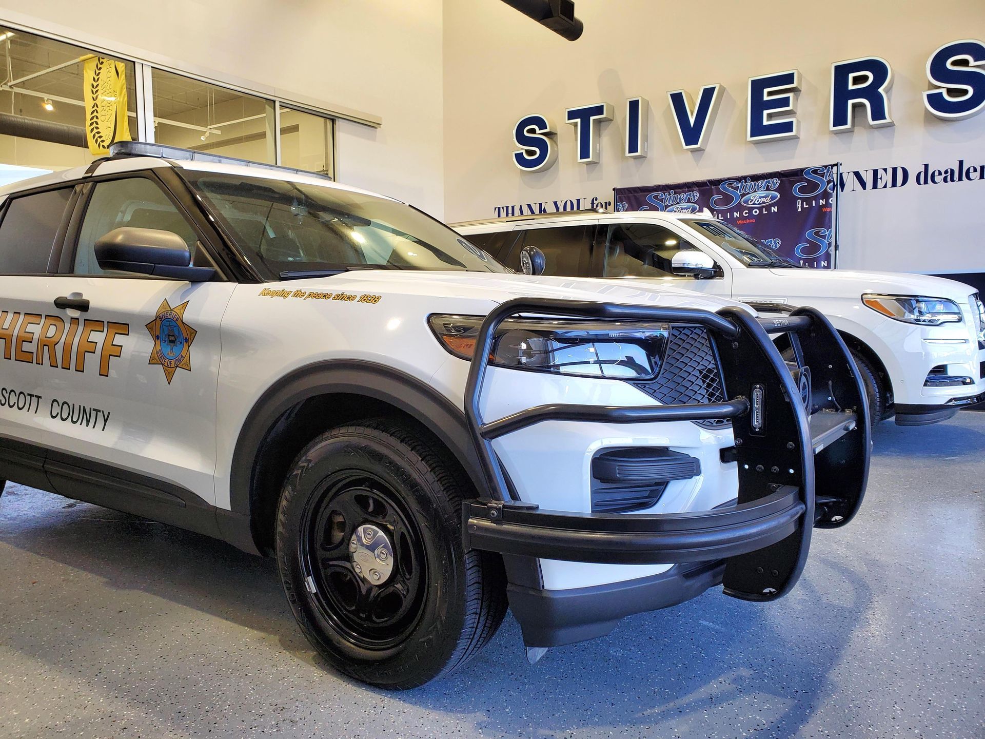 A sheriff 's car is parked in front of a dealership.