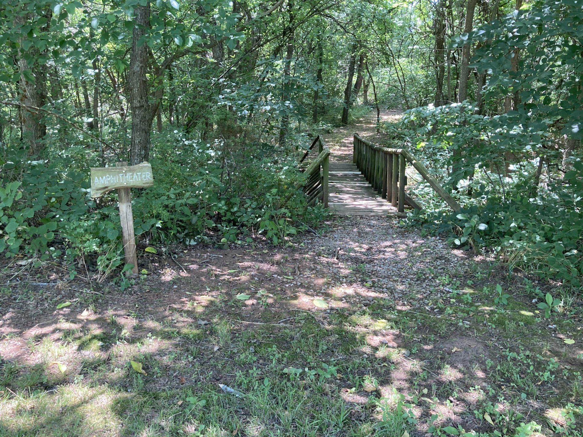 Trail entrance with a wooden bridge in a forest. A sign on the left.