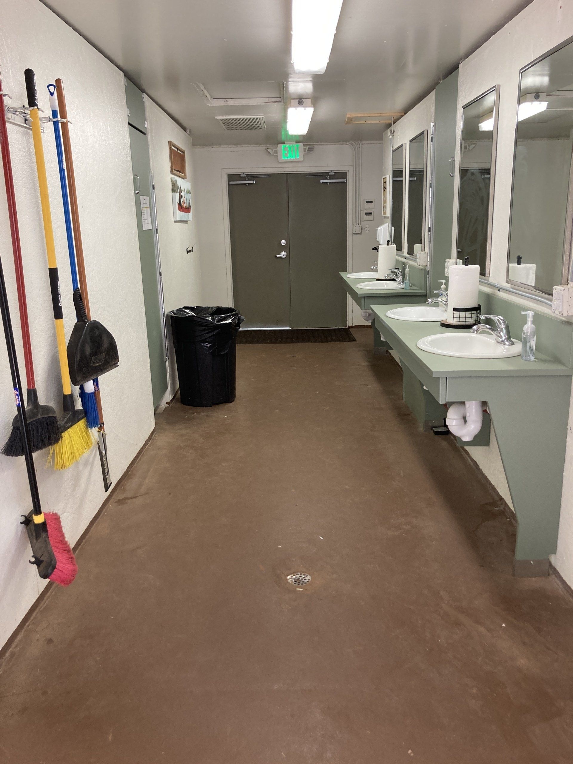 Public restroom with sinks, mirrors, brooms, and a doorway.