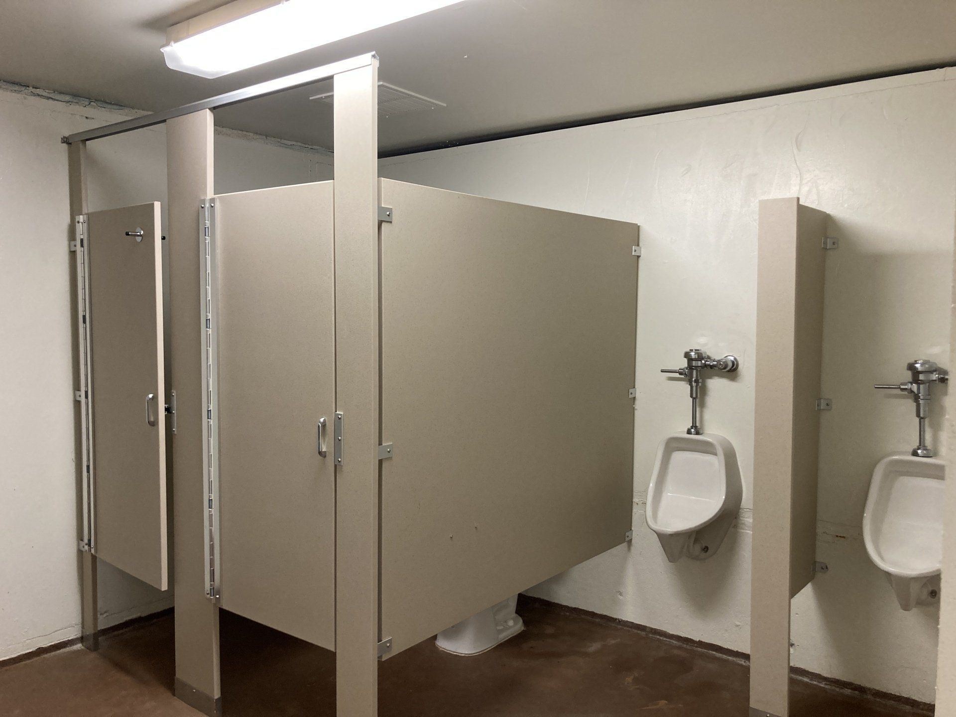 Public restroom with tan stalls and white urinals.